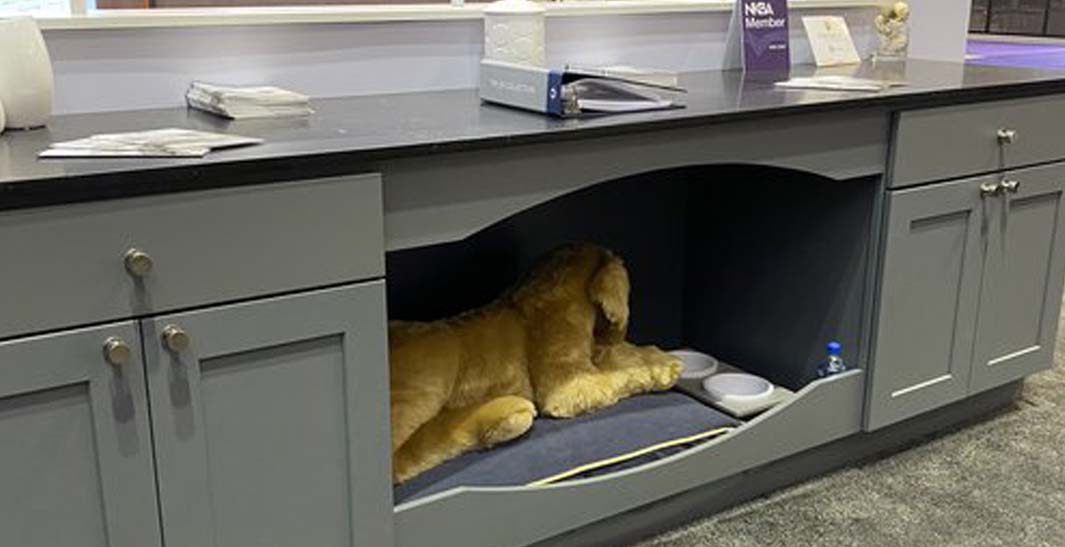 Plush dog toy in a cabinet nook, with a water bowl and a small bottle nearby on a gray carpeted floor.