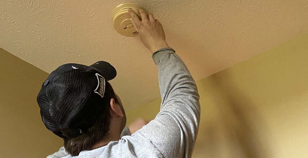 Person installing or checking a smoke detector on a ceiling.