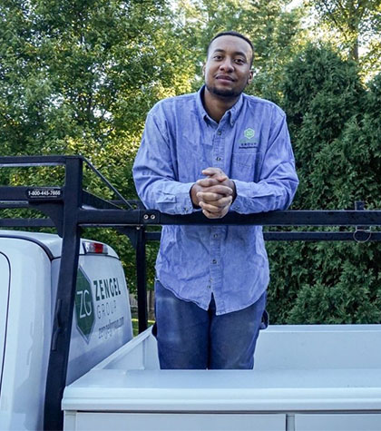 Man in a blue shirt stands in the back of a truck with a Zengel Group logo, surrounded by greenery.