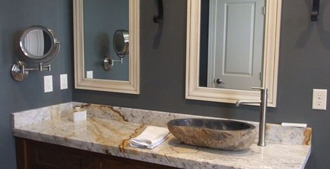 Bathroom with a marble countertop, a stone vessel sink, two framed mirrors, and a wall-mounted adjustable makeup mirror.