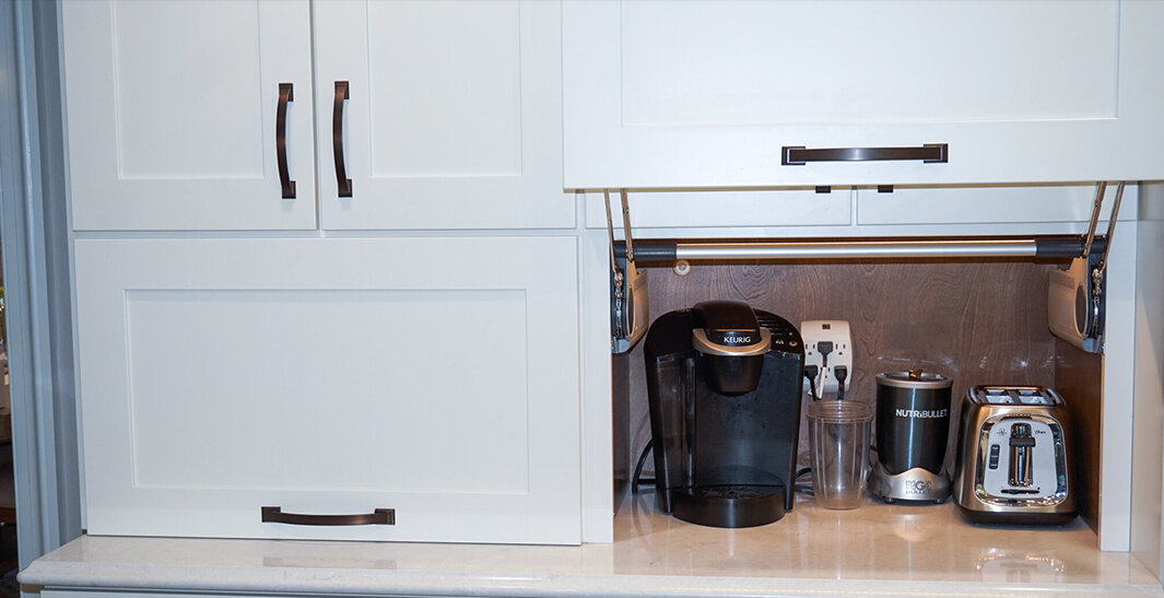 White kitchen cabinets with a pull-up door reveal a coffee maker, blender, and toaster on the countertop.