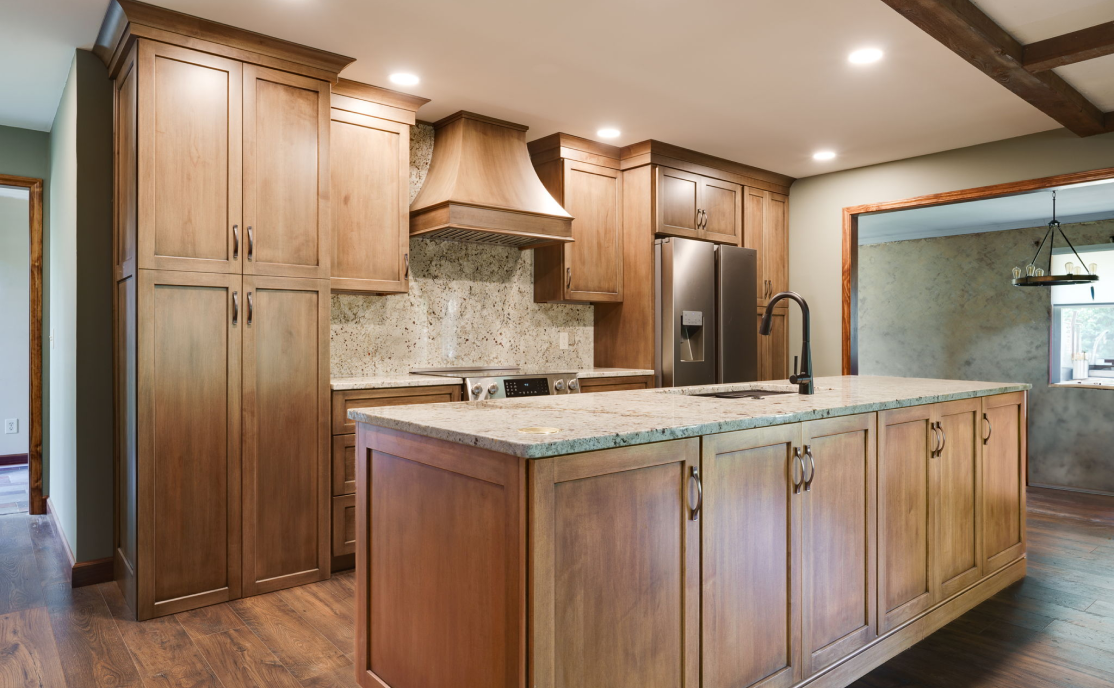 Modern kitchen with wooden cabinets, a central island with sink, stainless steel refrigerator, and marble countertops.