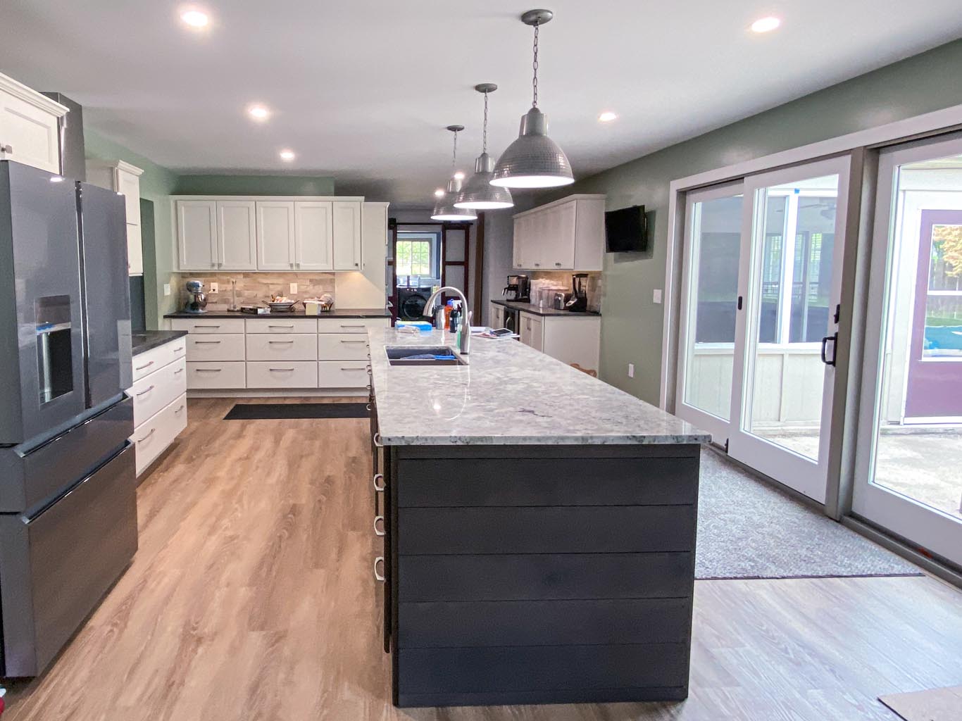 Spacious modern kitchen with a large island, stainless steel appliances, and white cabinets. Sliding glass doors lead to an outdoor area. Wood flooring enhances the contemporary look.