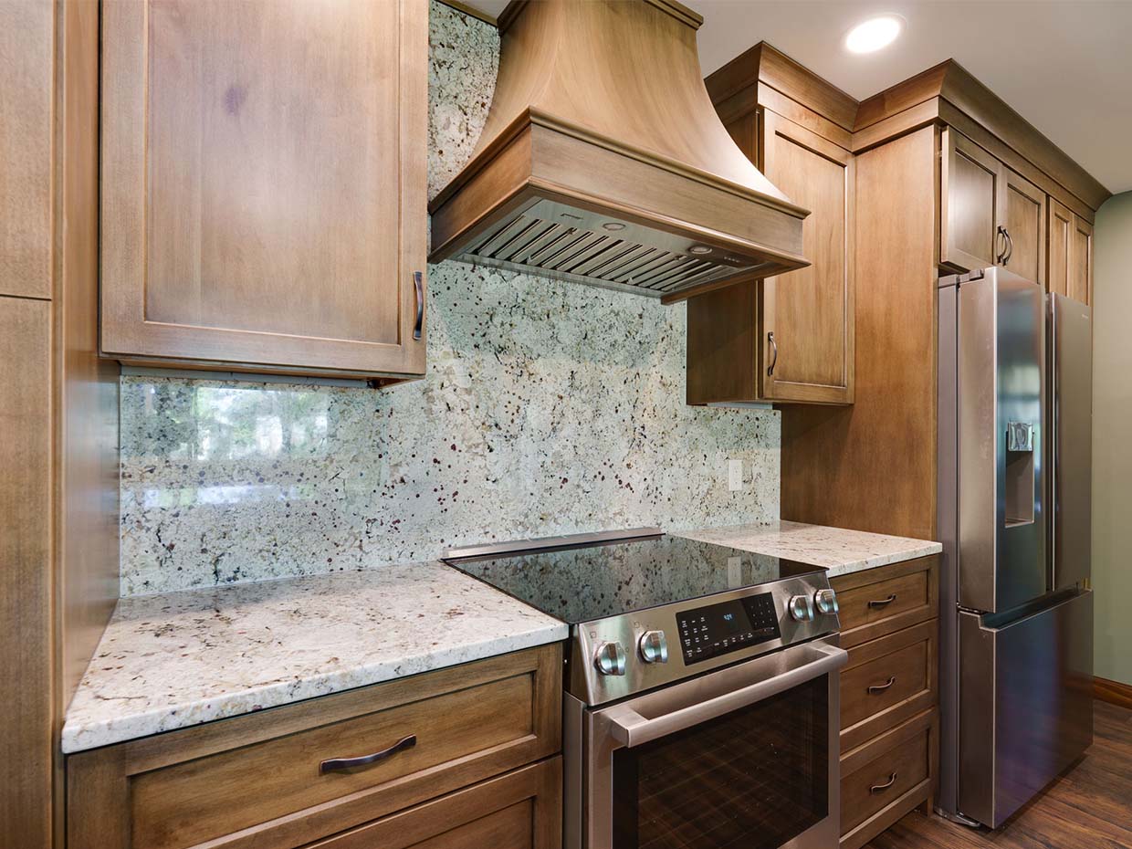 Modern kitchen with wood cabinets, stainless steel appliances, and granite countertops. Features a range hood above the stove and a refrigerator on the right.