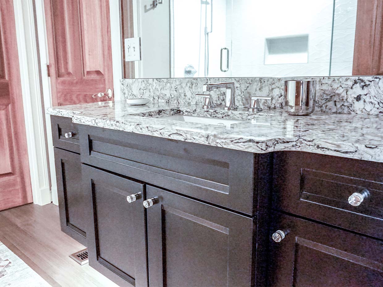 Bathroom with dark wood cabinets and a speckled granite countertop featuring a sink and modern chrome fixtures. A mirrored wall is above the counter.