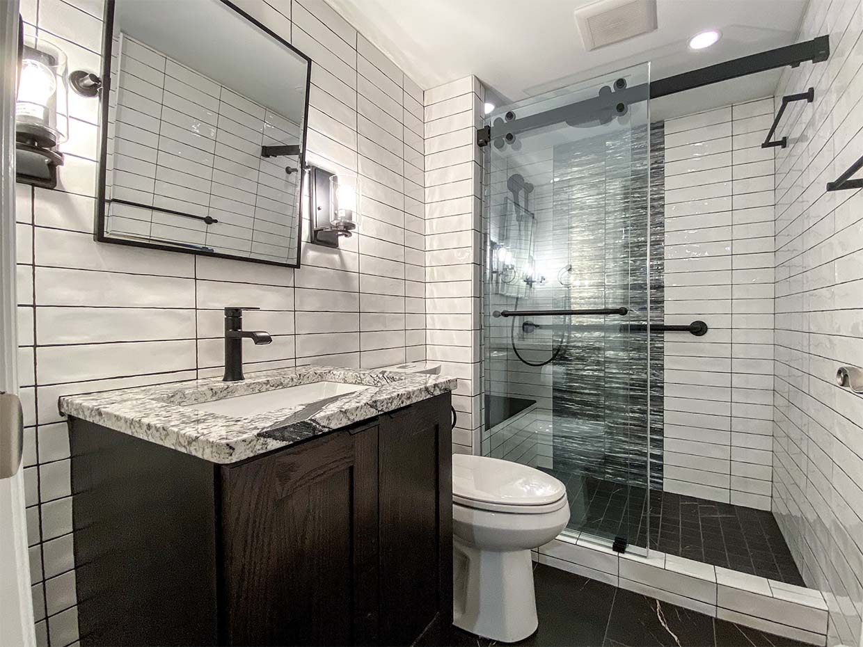 Modern bathroom with white subway tiles, black fixtures, glass shower door, and a granite countertop on a dark wood vanity.