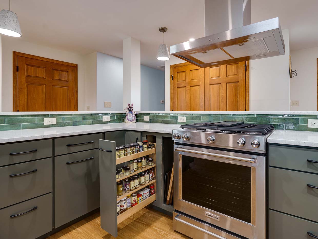 Modern kitchen with a silver stove, pull-out spice rack drawer, green cabinets, green tile backsplash, and wooden doors.