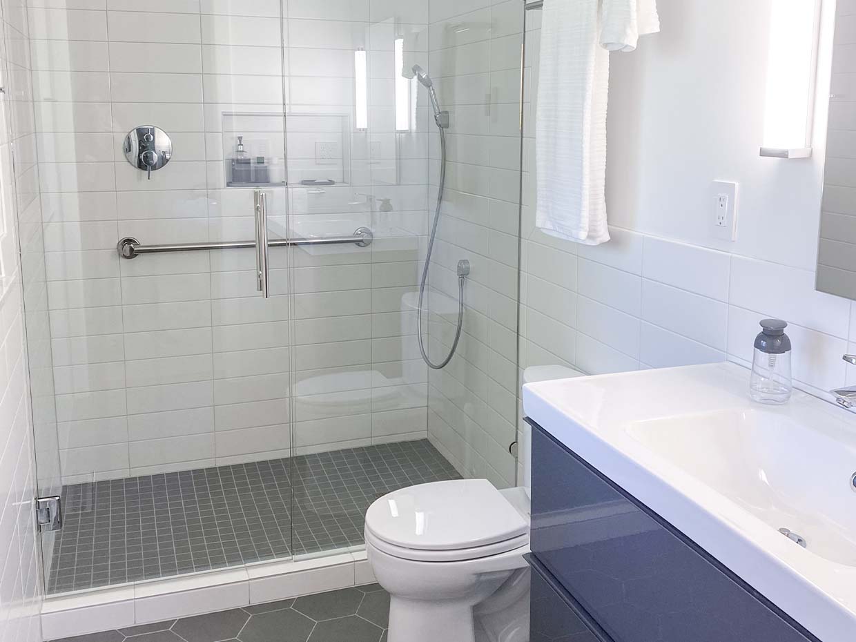 Modern bathroom with a glass-enclosed shower, white tiles, a wall-mounted towel, a toilet, and a sleek dark vanity with a sink.