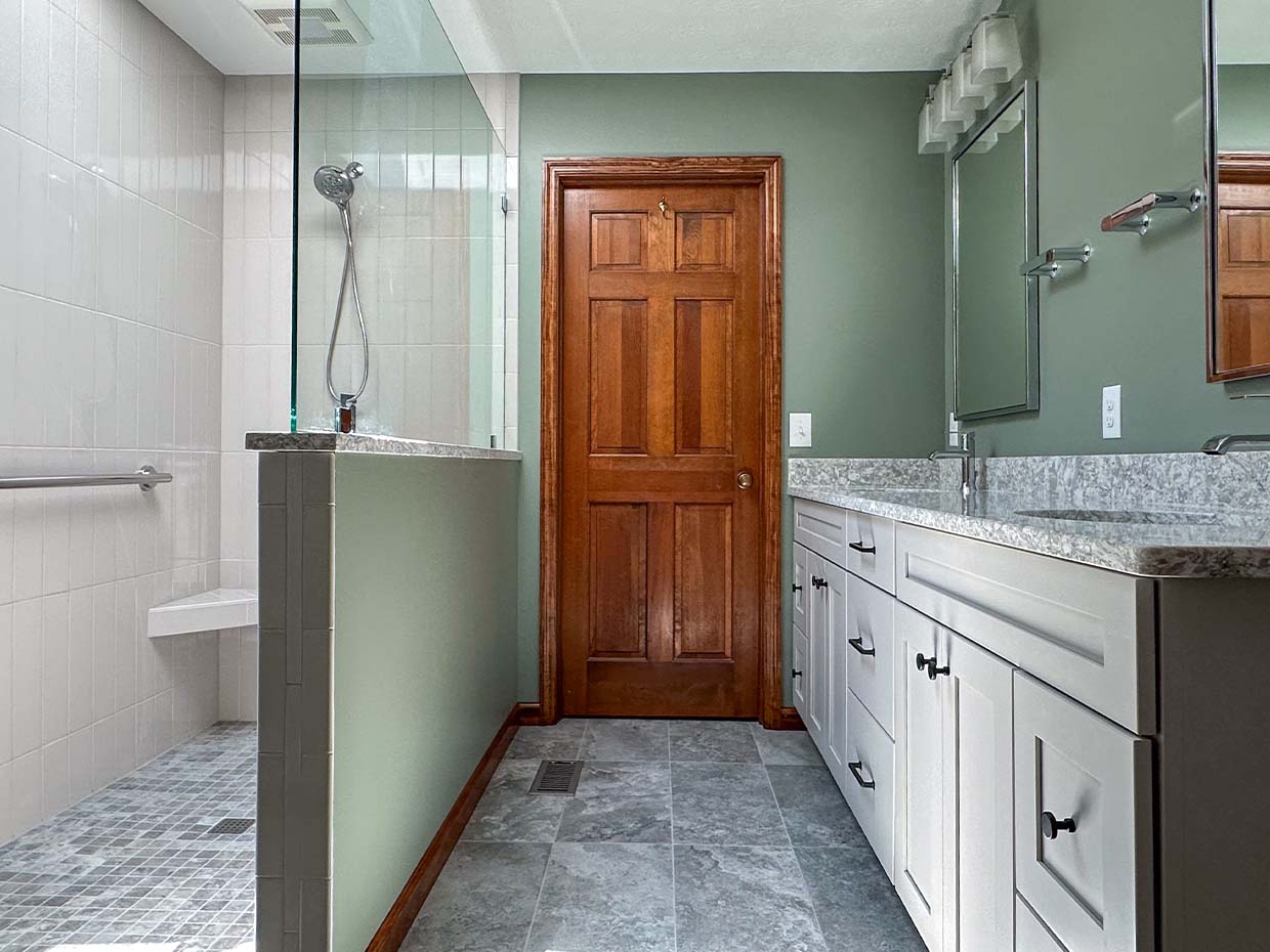 A bathroom features a walk-in shower, wooden door, and dual-sink vanity with granite countertop. The walls are green, and the floor is tiled.