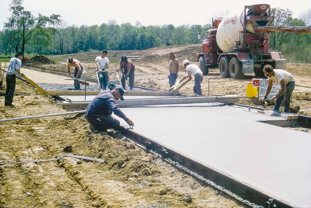 Workers pouring and smoothing concrete on a construction site with a cement truck in the background.