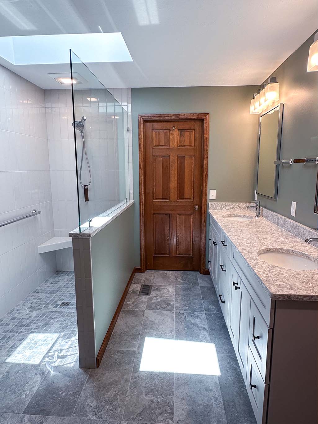 A bathroom with a wooden door, dual-sink vanity, and tiled shower area.