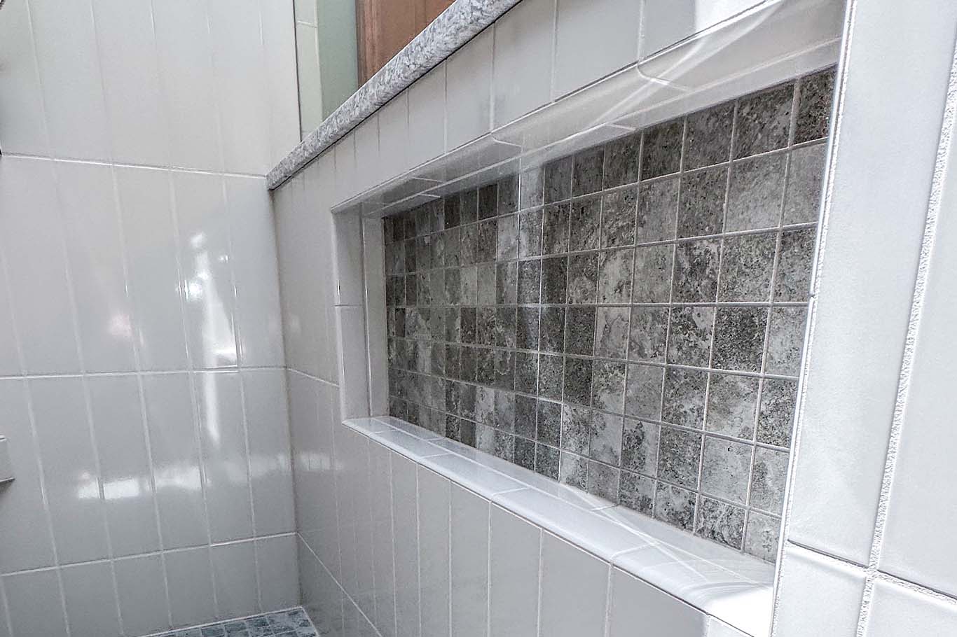 A tiled shower niche with a mix of gray and white tiles, featuring a recessed shelf.