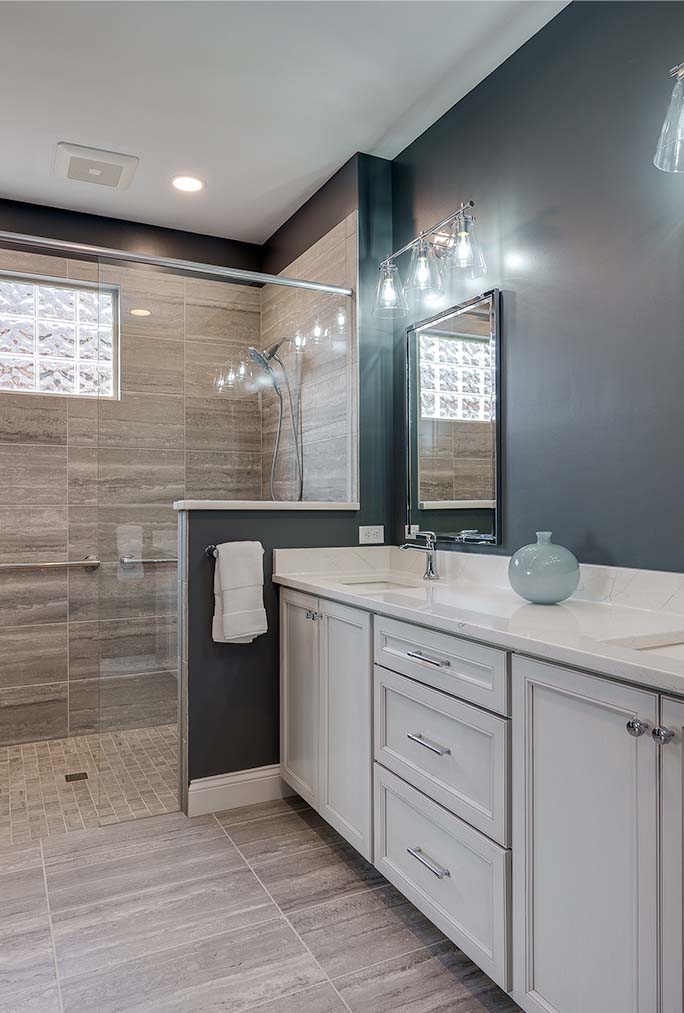 Bathroom Remodel Centerville OH Modern bathroom with gray tiled walk-in shower, glass partition, white vanity with drawers, large mirror, and a decorative vase on the countertop—perfect inspiration for your next home remodeling project.