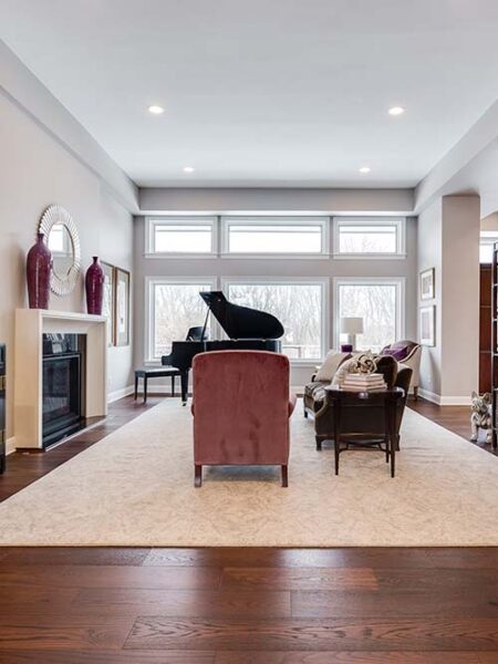A modern living room, perfect for home remodeling inspiration, features a grand piano, large windows, armchairs, a sofa, a fireplace, and decorative vases on the mantel.