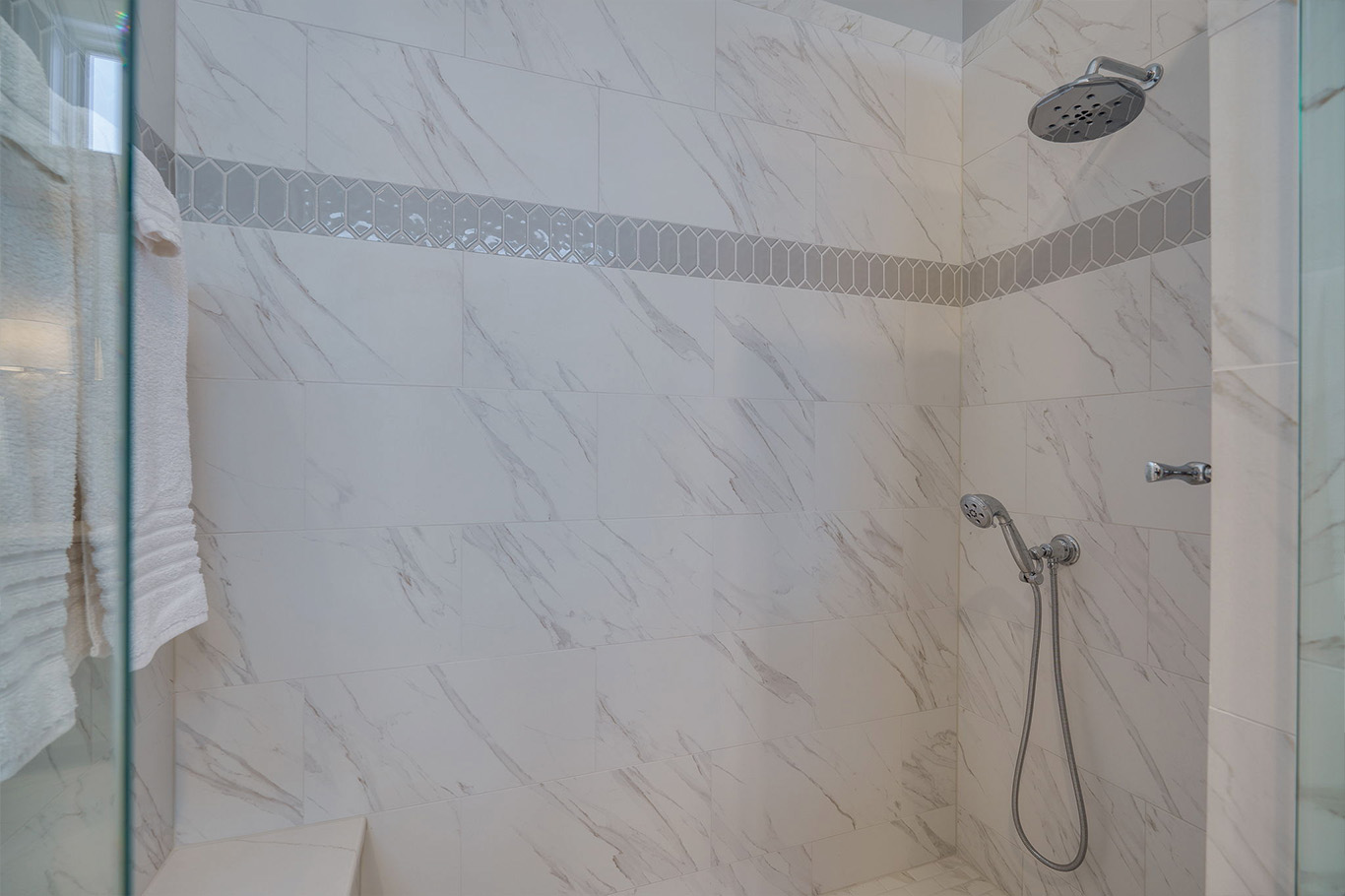 bathroom remodel service page 4 Modern tiled shower with white and gray marble-patterned walls, hexagon accent strip, overhead and handheld showerheads, plus a folded towel on the side—a perfect example of bathroom remodeling Dayton residents love.