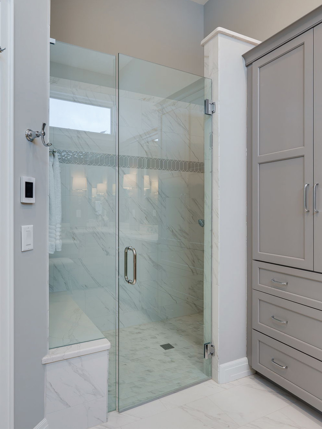 bathroom remodel service page Modern bathroom with a glass-enclosed shower featuring marble tile, a built-in bench, and gray cabinetry on the right—perfect inspiration for your bathroom remodeling Dayton project.