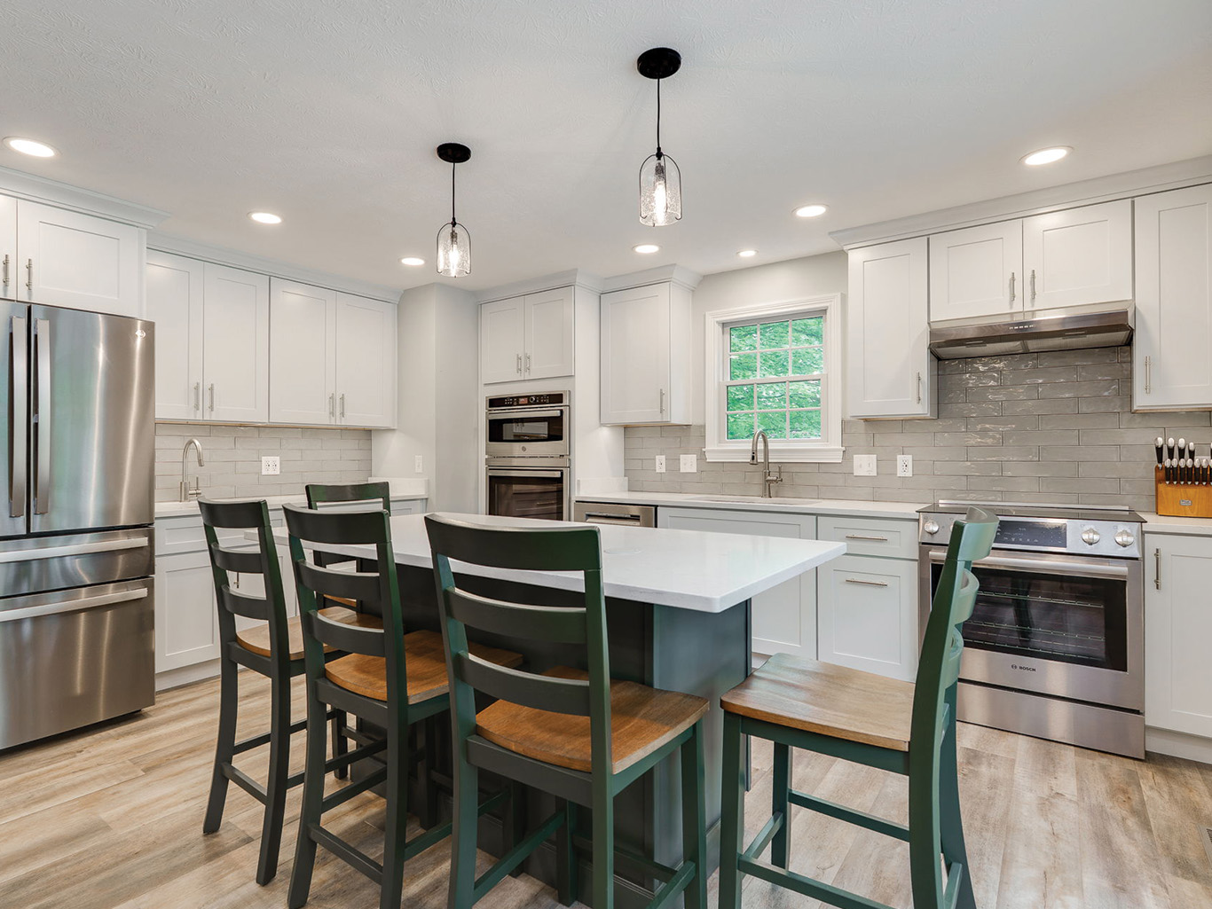 Modern kitchen with stainless steel appliances, white cabinets, gray tile backsplash, an island with green chairs, and two pendant lights above the island.