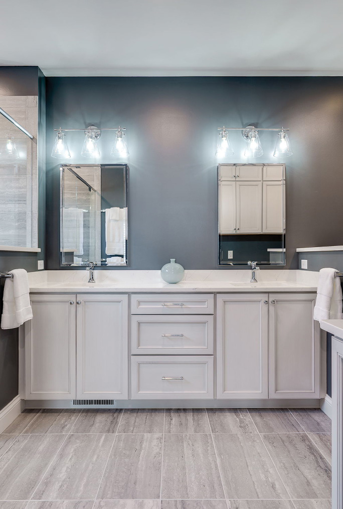 Modern bathroom with dual sinks, gray cabinets, matching mirrors, wall-mounted lights, and light gray tile flooring—perfect for your next home remodeling project.
