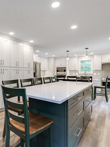 Modern kitchen with a large island, white cabinets, stainless steel appliances, wood flooring, and several chairs around the island—an ideal space for home remodeling inspiration.