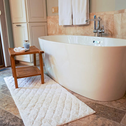 A bathroom with a freestanding bathtub, a wooden stool holding a towel and cup, a bath mat on the floor, and a digital scale nearby.