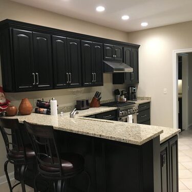 Modern kitchen with black cabinets, granite countertops, and bar seating. Includes stainless steel appliances and overhead lighting. Decor includes a small Santa figure on the counter.