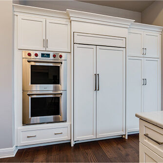 Built-in double oven, refrigerator, and cabinetry with white panel doors in a modern kitchen with wood floors and white countertops—explore our pricing guide for more details.